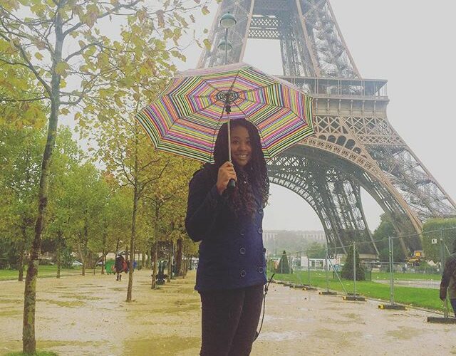 A woman standing in front of the eiffel tower holding an umbrella.