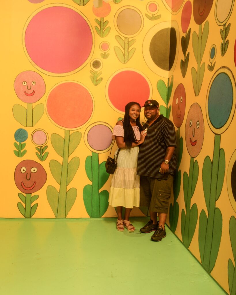 A man and woman standing in front of a wall with flowers on it.