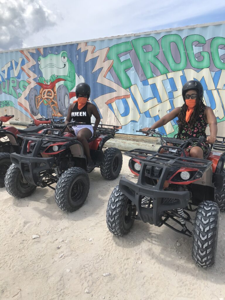 Two women sitting on four wheelers in front of a wall.