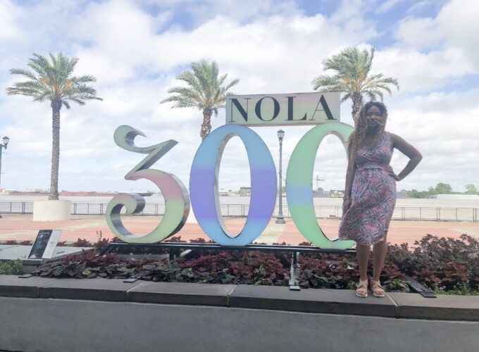 A woman standing in front of a sign that says " nola 3 0 0 ".